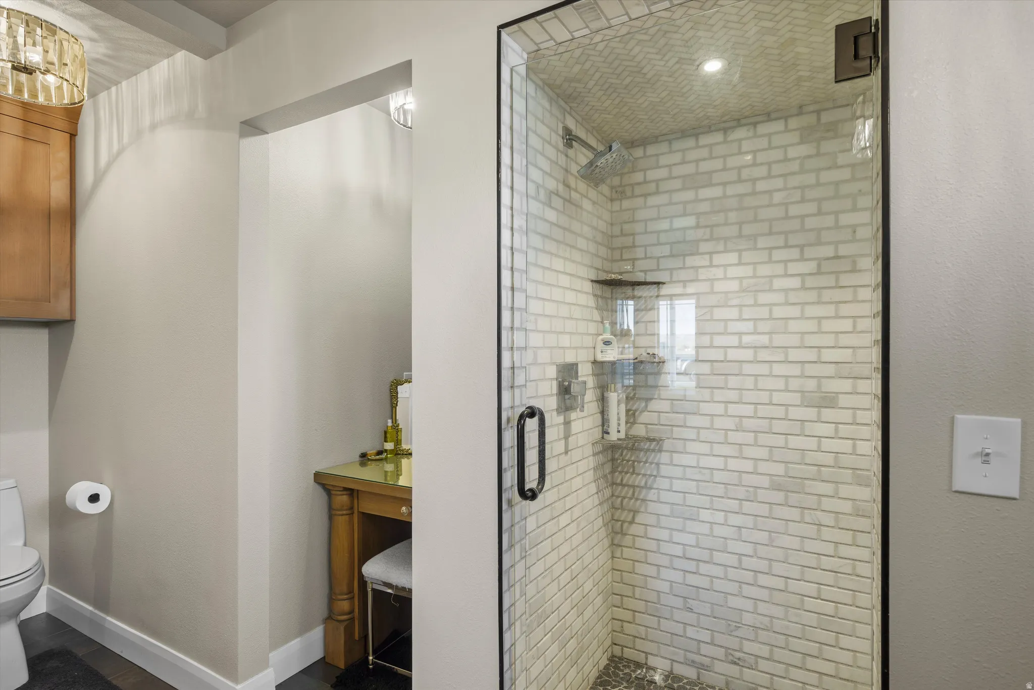 Walk-in shower featuring subway tile surround, pebble tile flooring, and glass enclosure with dark trim