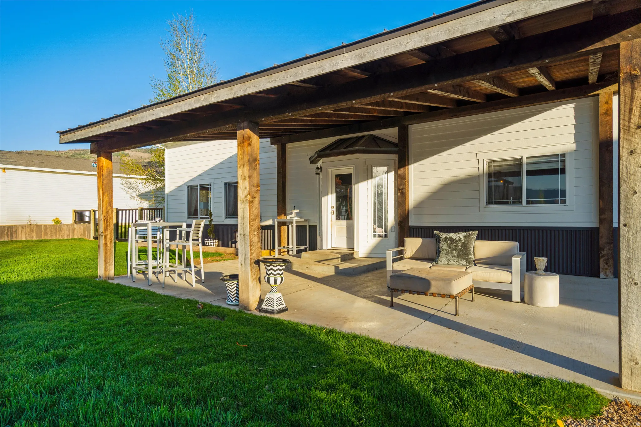 Covered concrete patio with exposed wood beam ceiling, wood support columns, white panel siding, and a white entry door