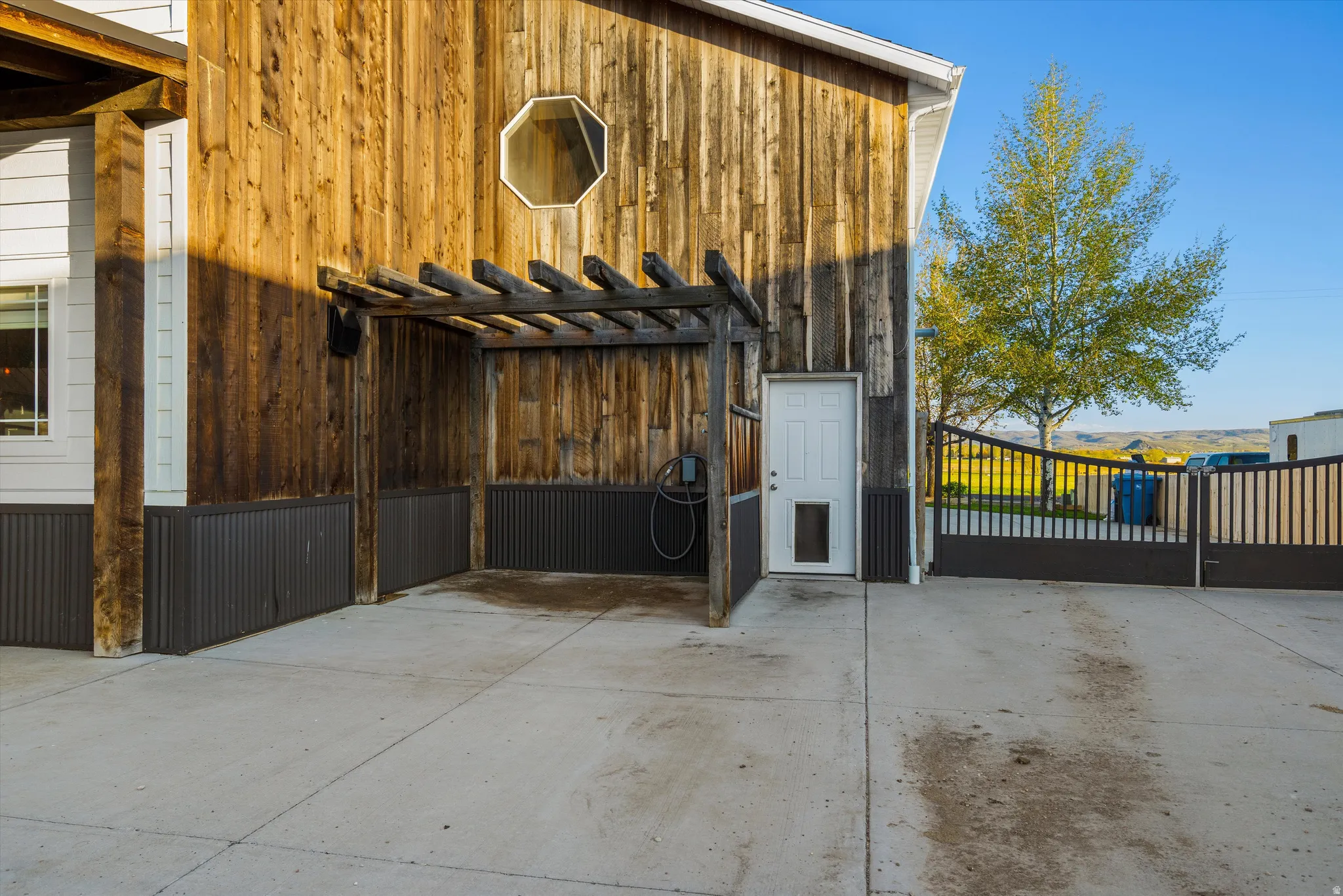 Exterior featuring natural wood siding, an octagonal window, white entry door, and a built-in pergola structure