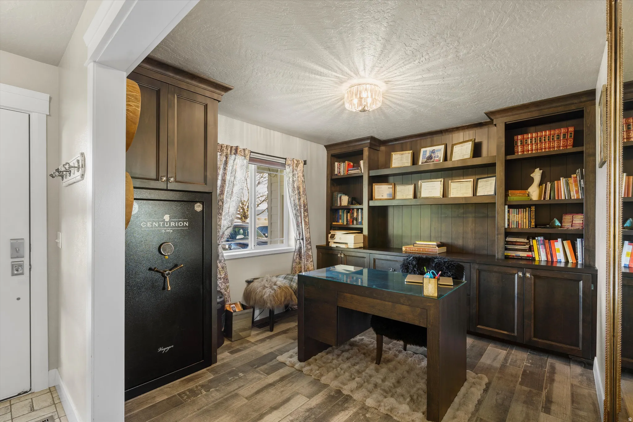 Dedicated office space featuring built-in cabinetry and shelving, a wood-finish desk with a glass top, and wood-finish flooring