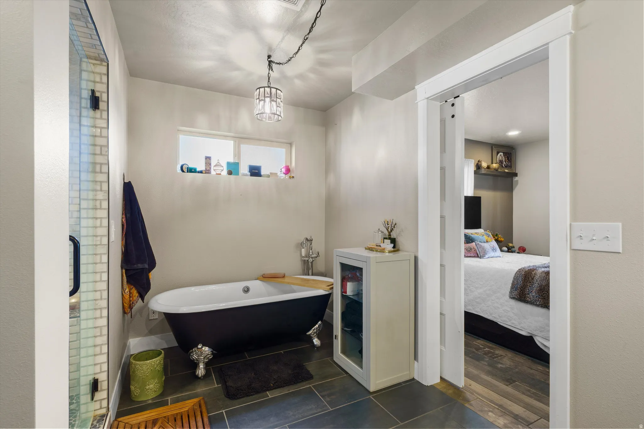Bathroom featuring a standalone clawfoot tub, a glass-enclosed shower, slate tile flooring, and a crystal chandelier