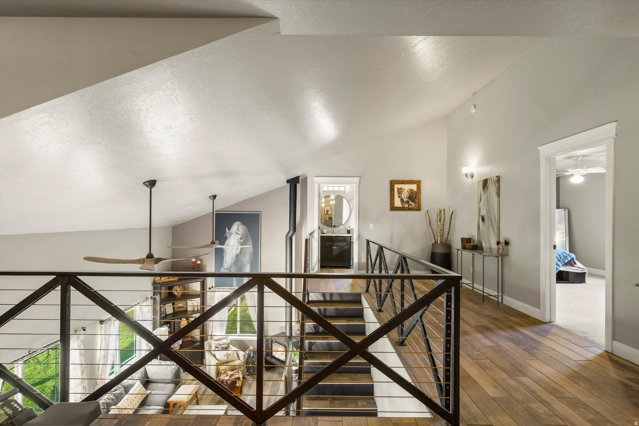 Open upper-level walkway featuring wood-finish flooring, a contemporary black metal and cable railing, vaulted ceilings, and recessed lighting