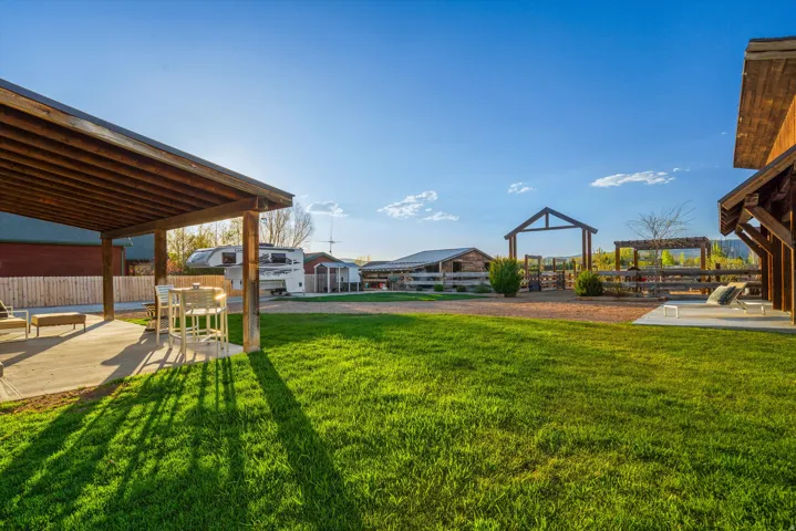 Expansive outdoor space featuring a covered patio, a large grassy area, a gravel pathway, a wooden pergola, and a visible barn structure