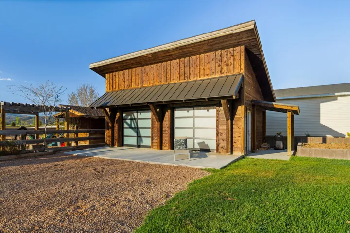 Modern barn-style structure featuring vertical wood siding, a standing seam metal roof, and two frosted glass overhead doors