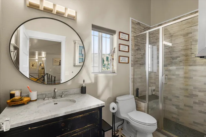 Bathroom featuring a dark wood vanity with a white stone countertop, a round black-framed mirror, and a glass-enclosed shower with stone tile walls
