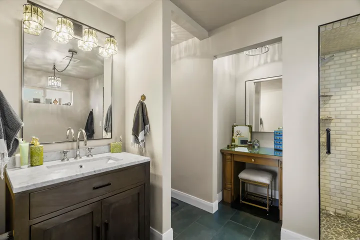 Bathroom featuring a dark wood vanity with a white countertop and a rectangular undermount sink, a large mirror with integrated lighting, and a glass-enclosed shower with subway tile walls