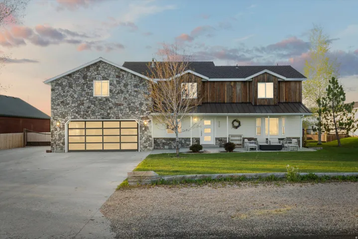 Stone and wood-sided exterior featuring a modern glass panel garage door, covered front porch, white door with vertical glass inserts, and a manicured lawn