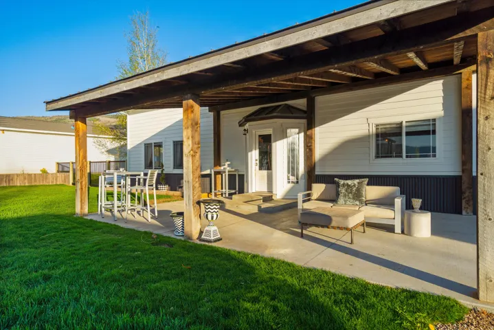 Covered concrete patio with exposed wood beam ceiling, wood support columns, white panel siding, and a white entry door