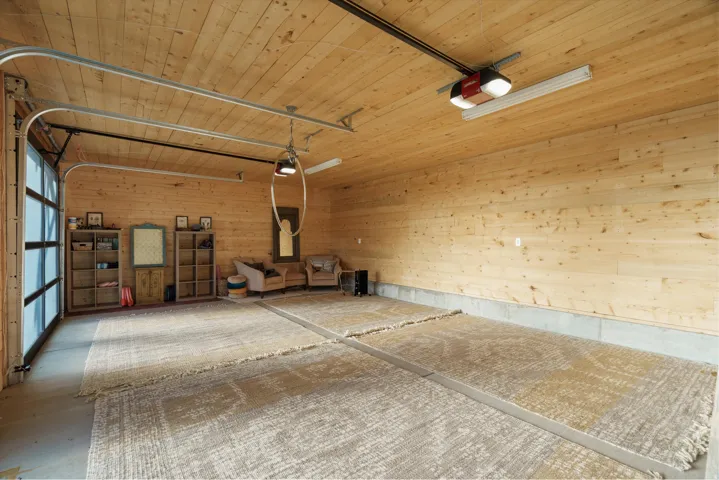 Spacious interior featuring natural wood plank walls and ceiling, a full-panel glass garage door, and durable concrete flooring with distinct sections