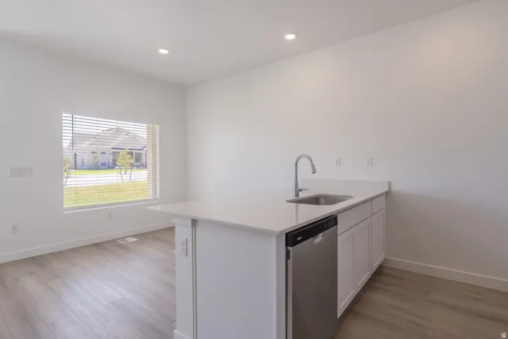White cabinetry, stainless steel dishwasher, undermount sink, gooseneck faucet, and light wood-finish flooring