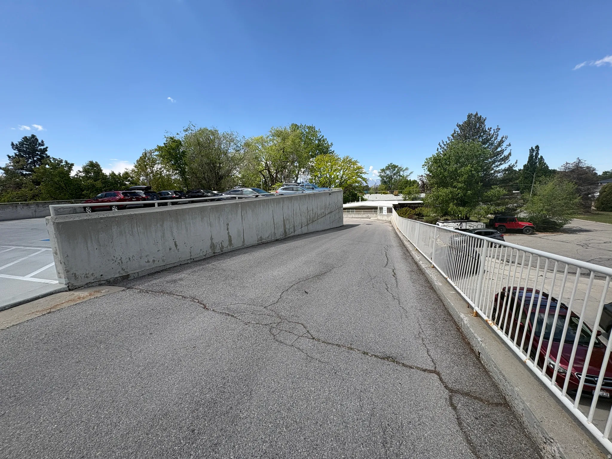Asphalt parking lot featuring a concrete retaining wall and a white metal railing