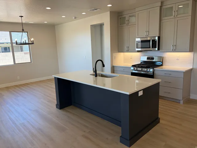 Open-concept kitchen with a large central island, light wood-finish flooring, recessed lighting, and a modern chandelier