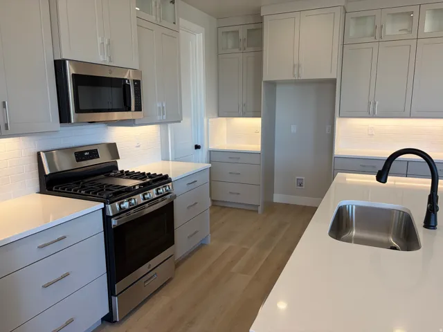 Kitchen featuring light-toned cabinetry, stainless steel appliances, white subway tile backsplash, light countertops, and wood-finish flooring