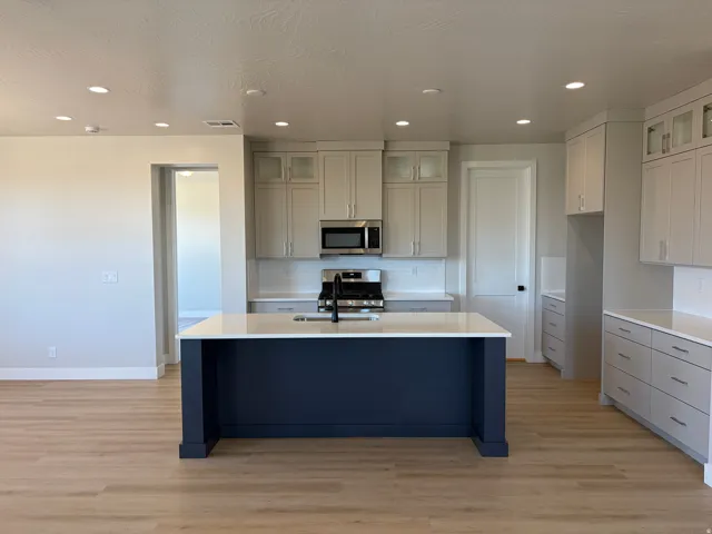Kitchen featuring a central island with white countertop, light wood-finish flooring, recessed lighting, and light grey cabinetry with stainless steel appliances
