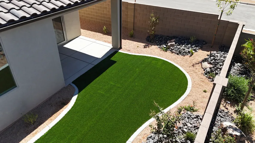 Private backyard featuring a covered patio, artificial turf lawn, and low-maintenance xeriscape landscaping with decorative rock