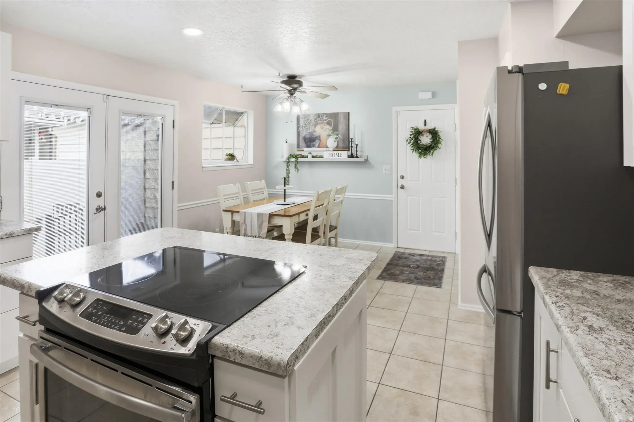 Kitchen featuring an island with built-in range, light-toned tiled flooring, white cabinetry, and granite-look countertops