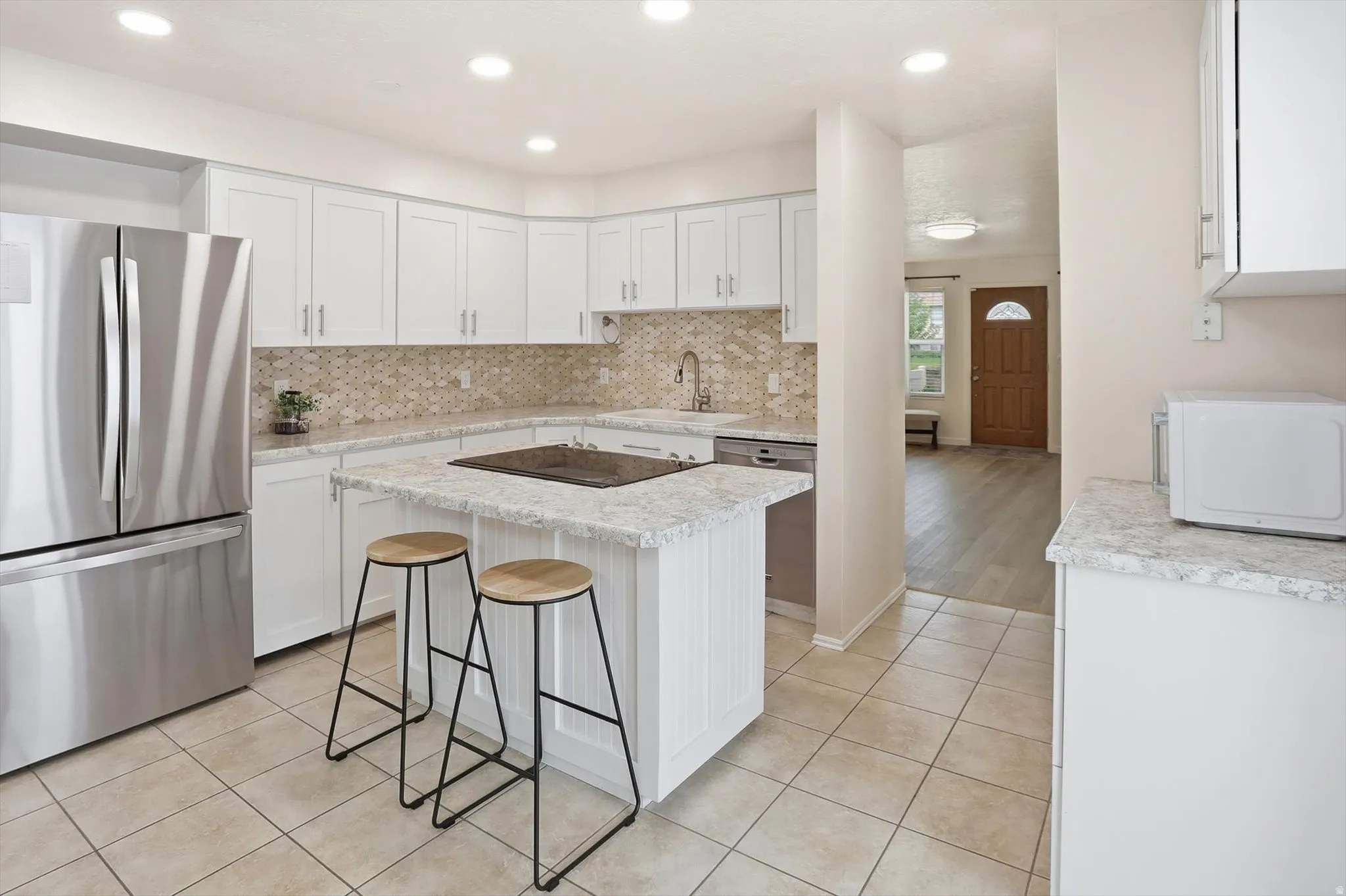 Modern kitchen featuring white cabinetry, light-colored countertops, a tile backsplash, stainless steel appliances, and a central island with an integrated cooktop