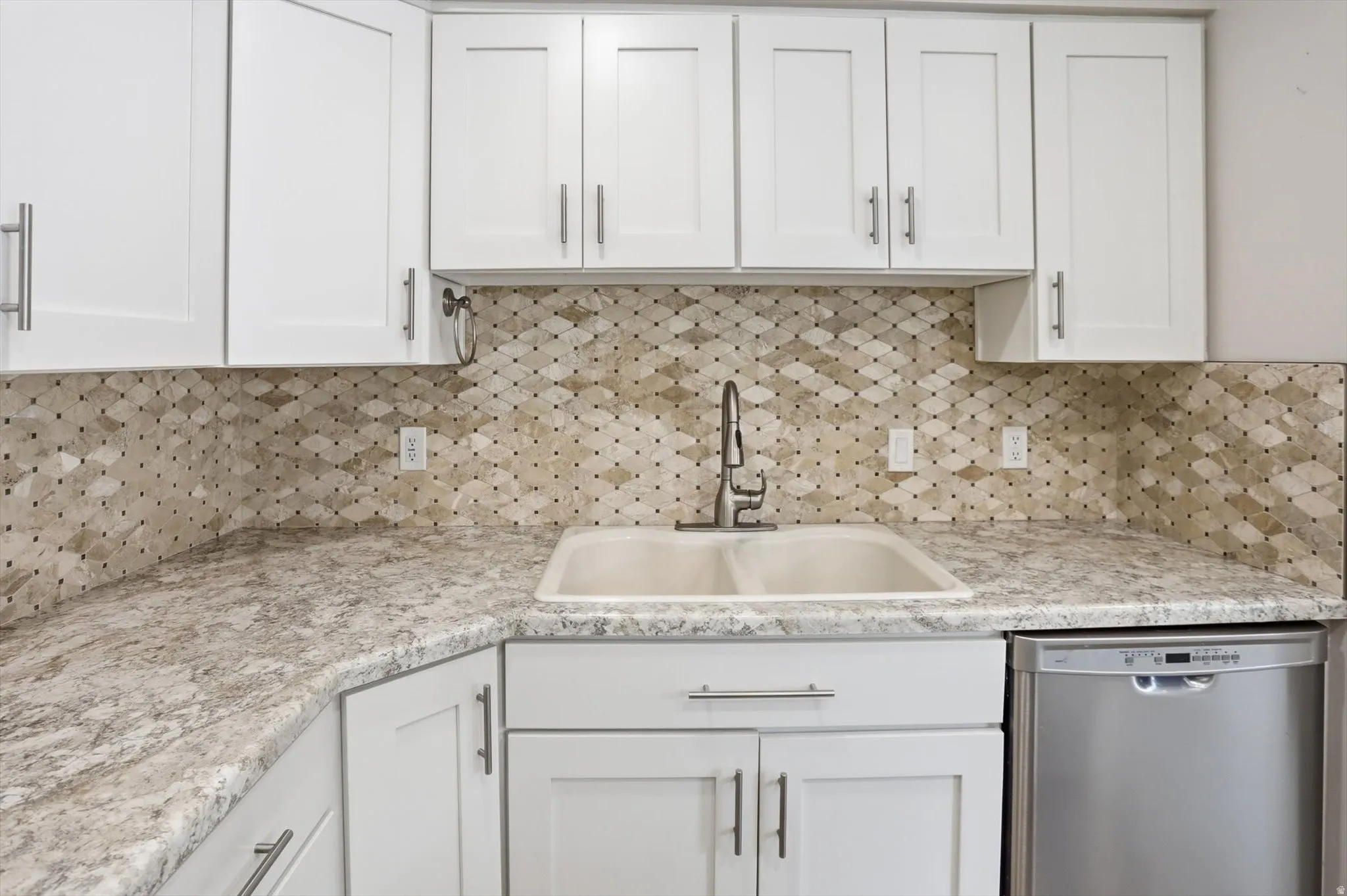Kitchen featuring white shaker-style cabinetry, a patterned tile backsplash, light-toned countertops, and a dual-basin sink with a pull-down faucet