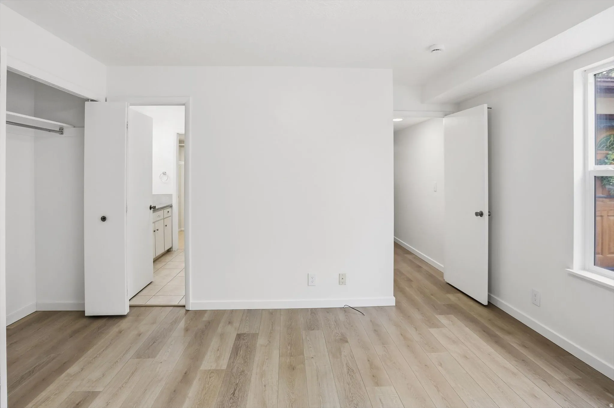 Spacious room featuring wood-finish flooring, white walls, and a window with exterior visibility