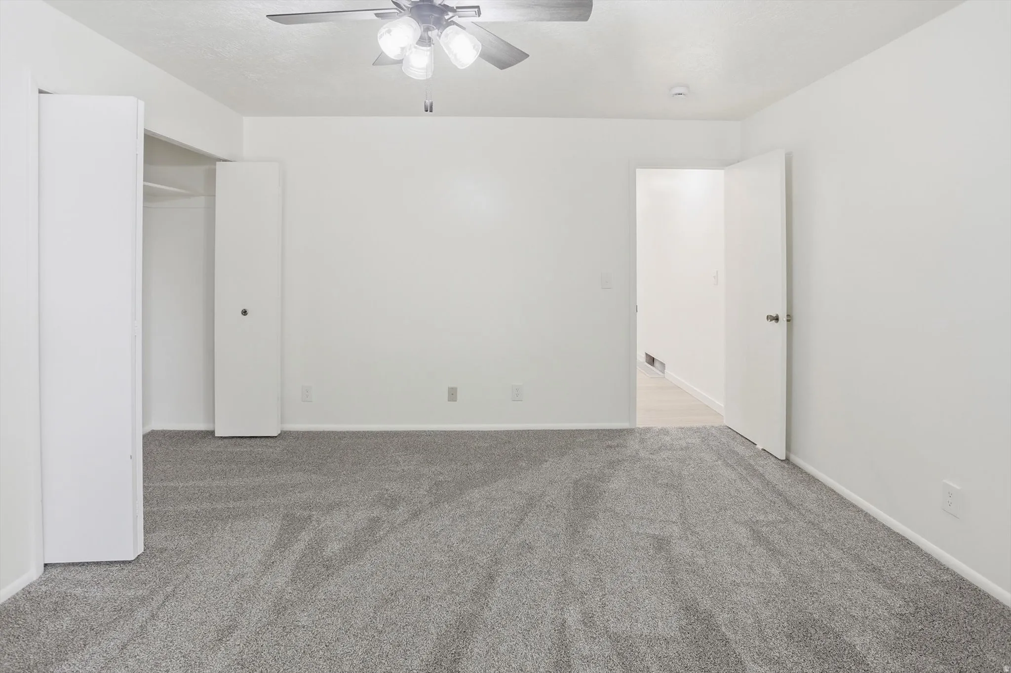 Spacious room featuring light gray carpeting, neutral white walls, and a ceiling fan with integrated lighting