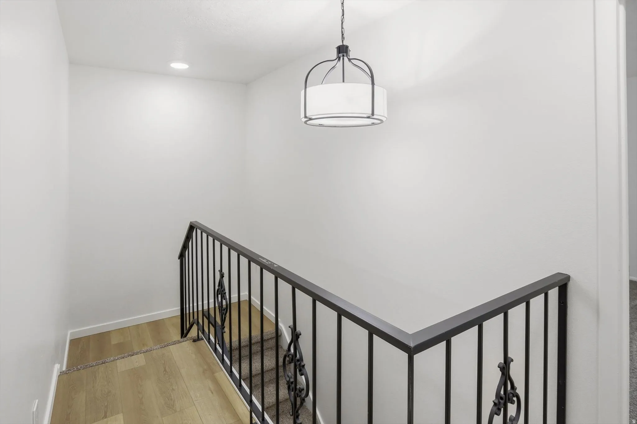 Staircase with wood-finish landing, wrought iron railing with decorative scrollwork, and a modern drum pendant light