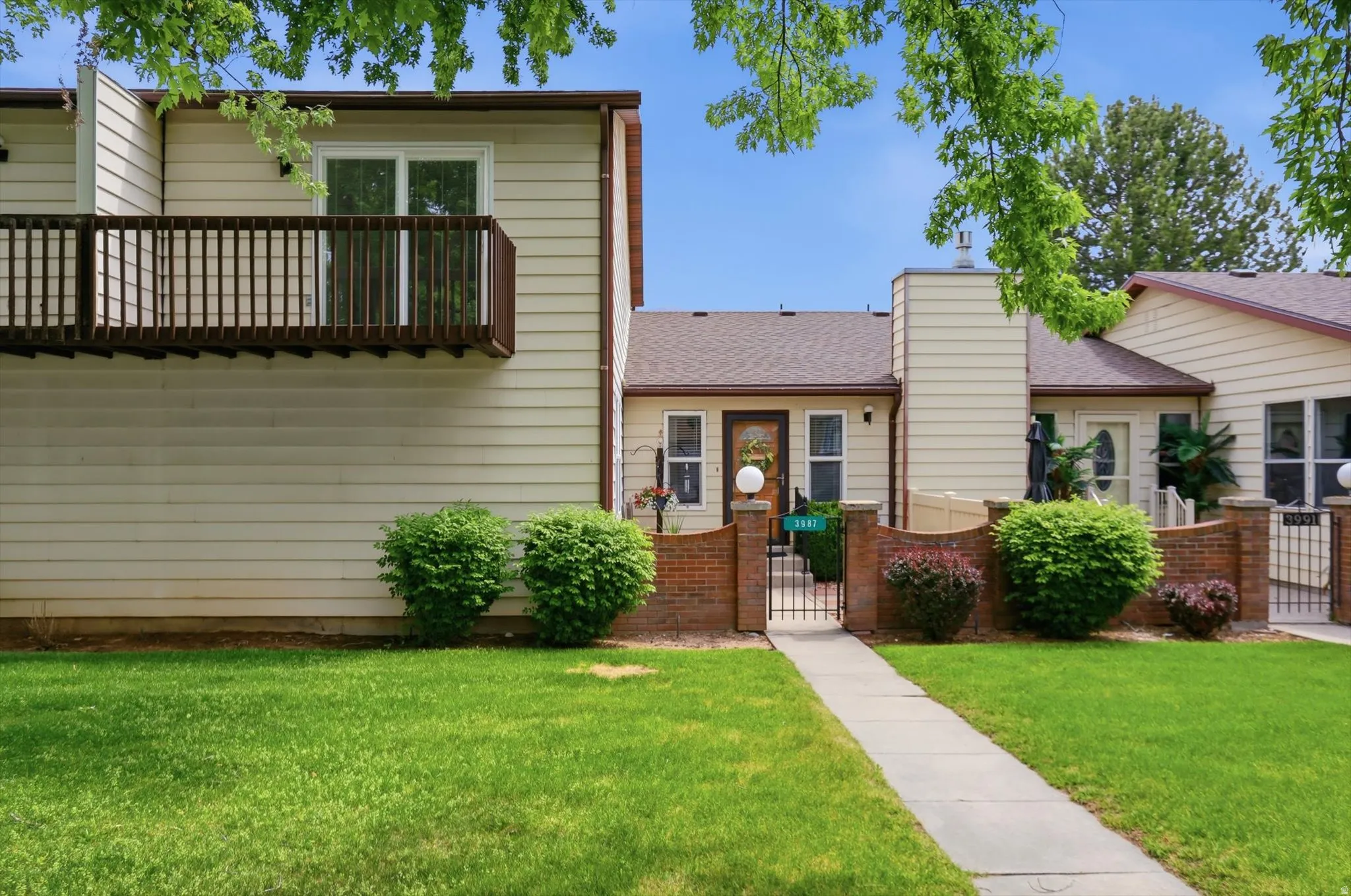 Property exterior featuring light-colored siding, a second-story balcony with dark wood railing, and a ground-level walkway