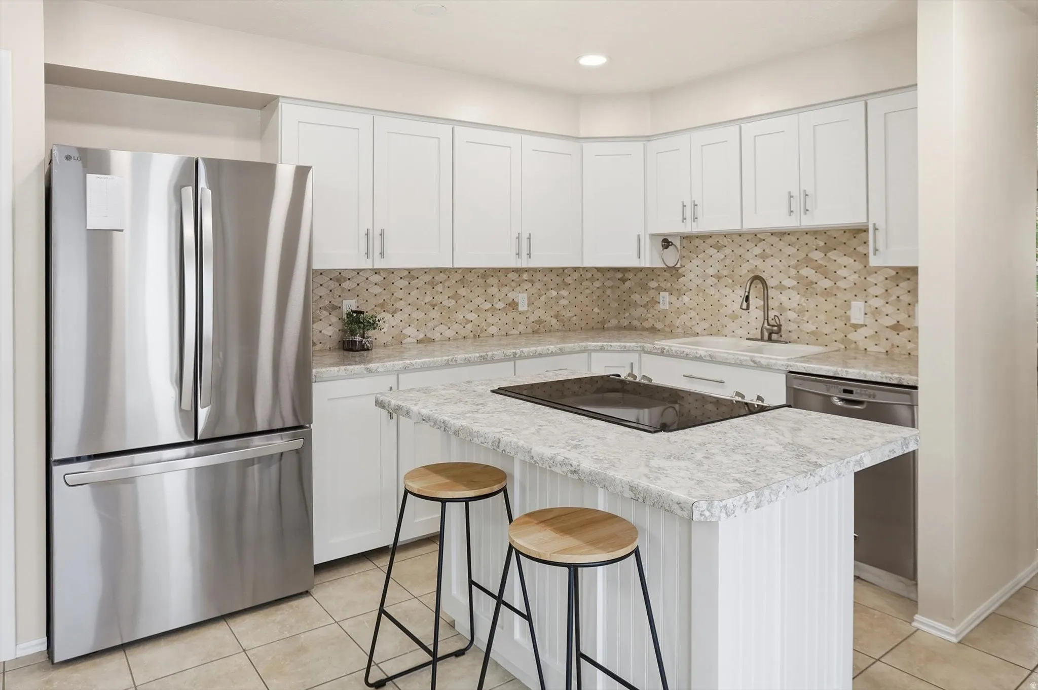 Contemporary kitchen featuring an island with a built-in cooktop, white shaker cabinetry, stainless steel appliances, mosaic tile backsplash, and light-toned countertops