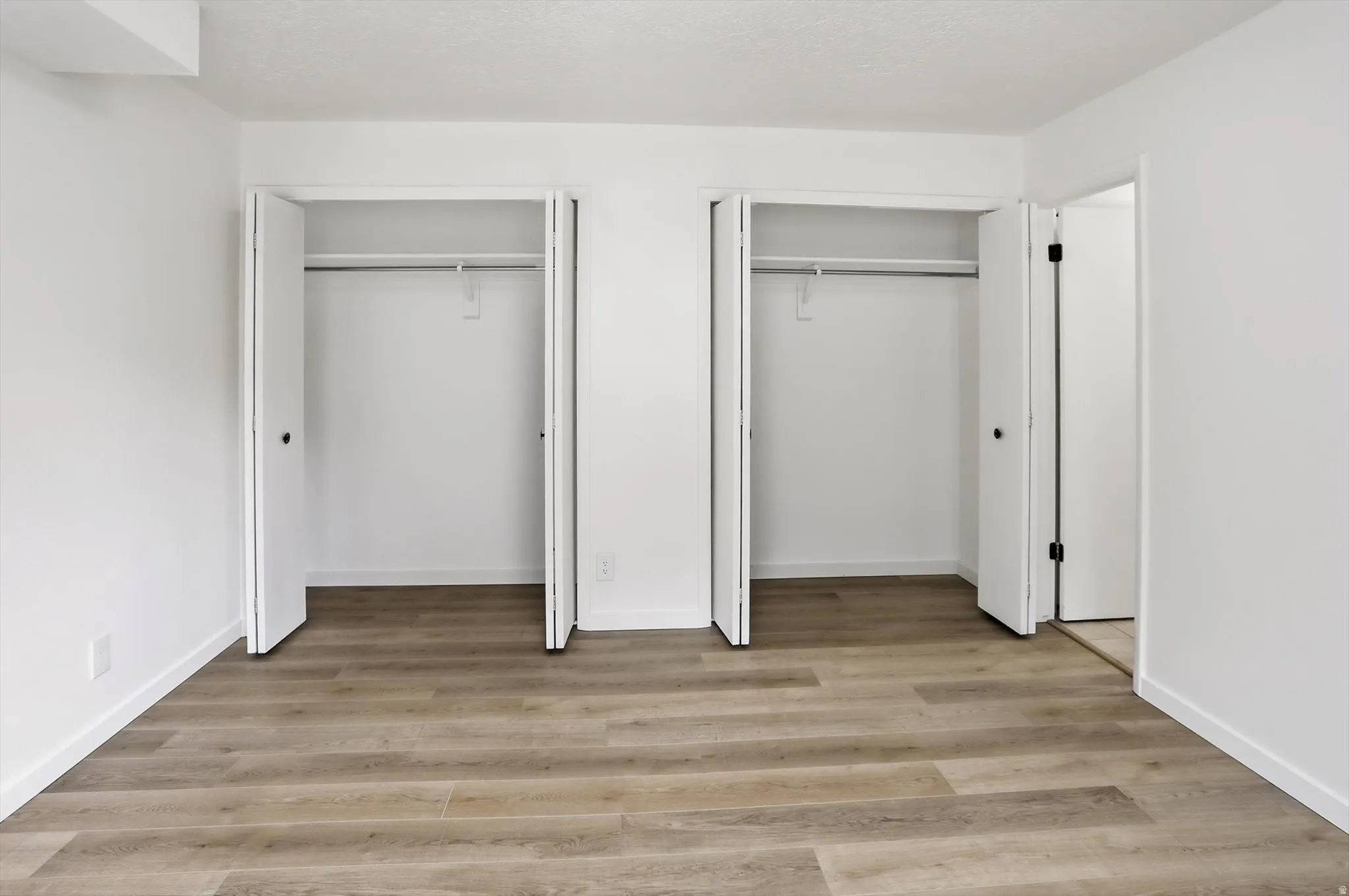 Room with wood-finish flooring, white walls, and white baseboards