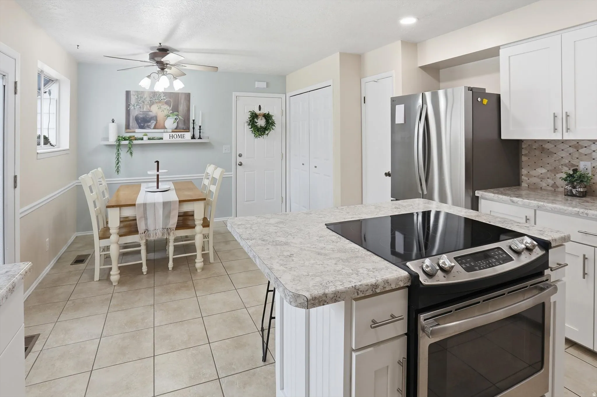 Integrated kitchen and dining area featuring a built-in cooktop, stainless steel refrigerator, white cabinetry, light-toned countertops, and neutral tile flooring