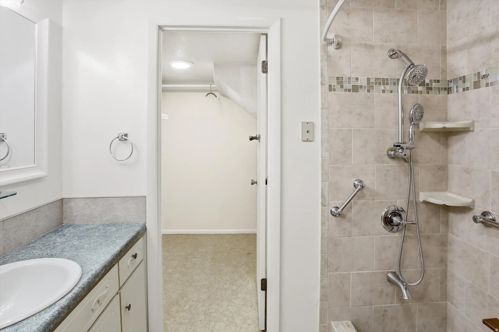 Bathroom featuring a tiled shower with mosaic accent band, multiple shower heads, and built-in shelving