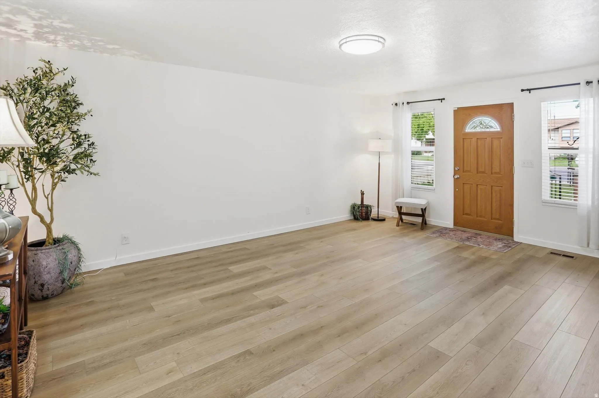 Bright living space featuring wood-finish flooring, a paneled entry door with an arched window, and multiple windows with blinds and sheer curtains