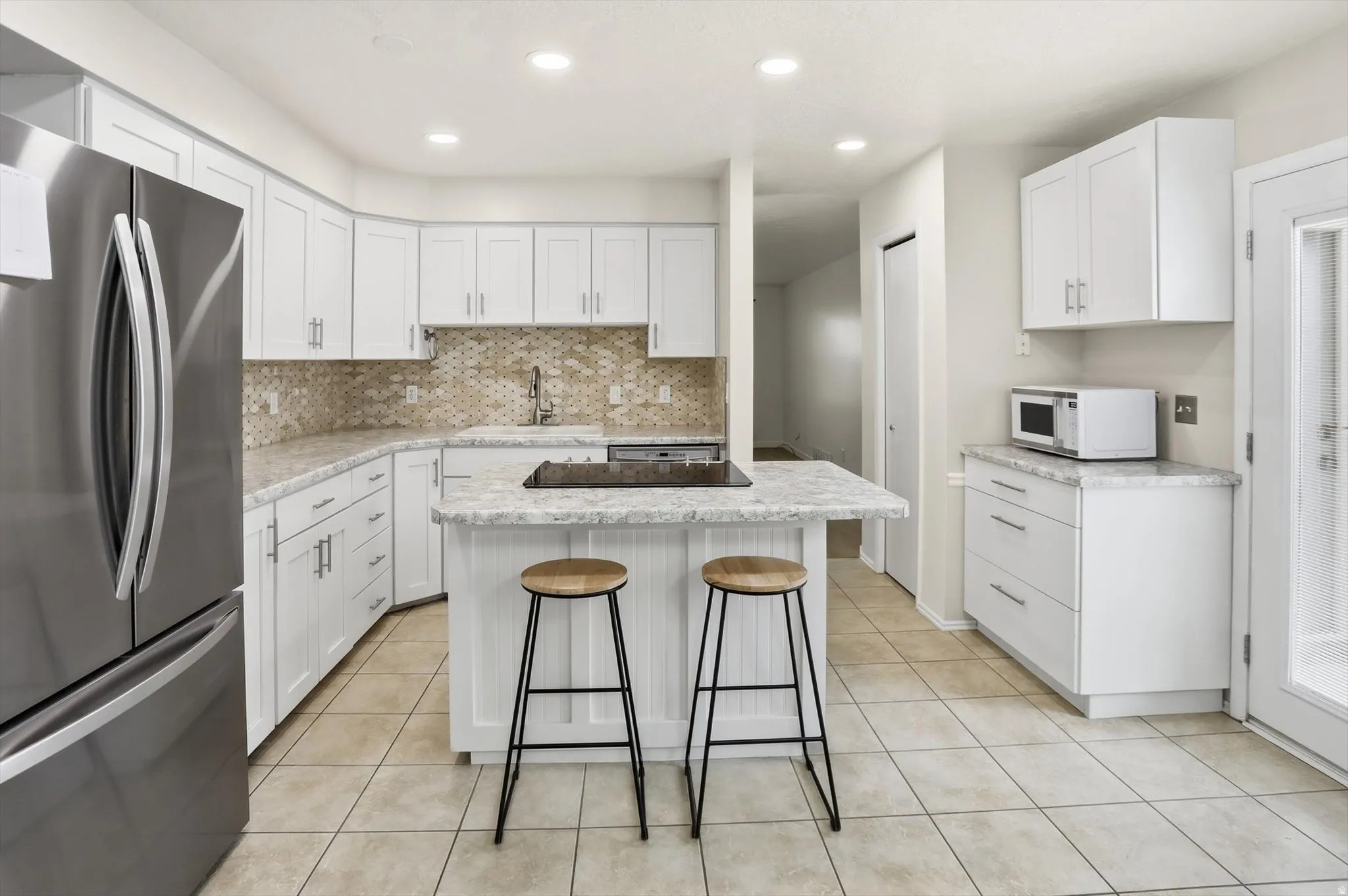 Modern kitchen featuring white cabinetry, light-toned countertops, a textured backsplash, and tiled flooring
