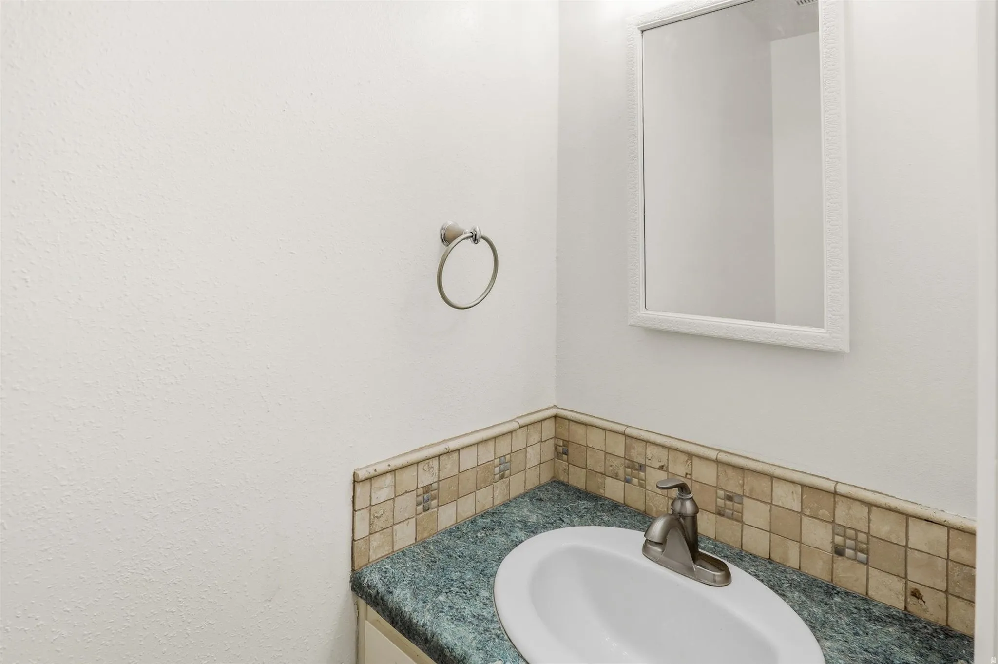 Vanity featuring an oval undermount sink with a brushed nickel faucet, a green speckled countertop, and a mosaic tile backsplash