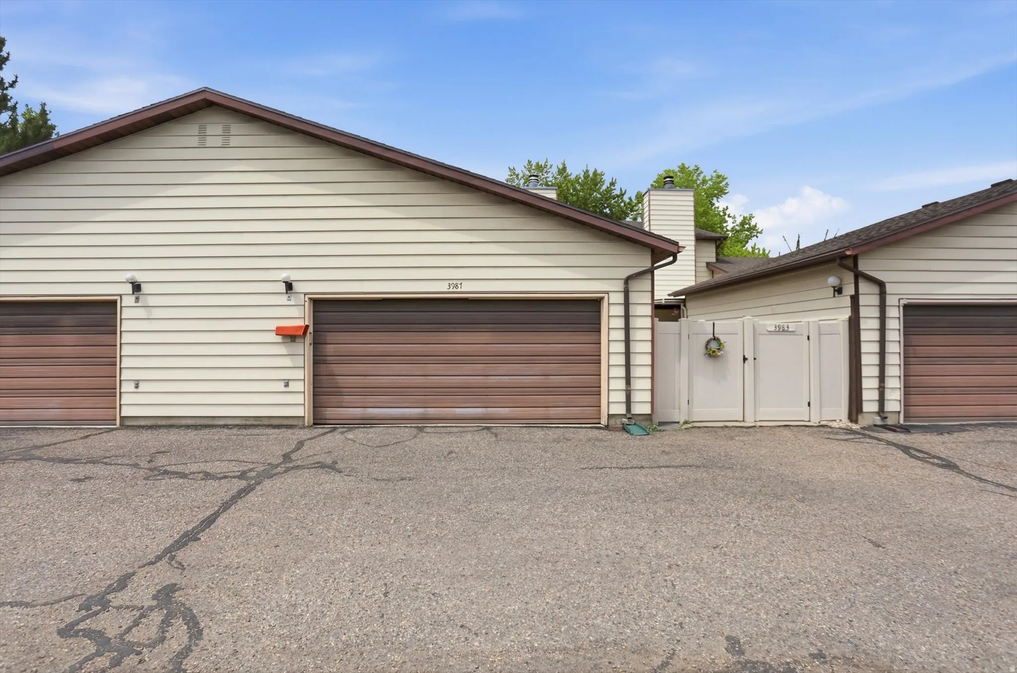 Exterior featuring light beige siding, two brown garage doors, and a partial white privacy fence