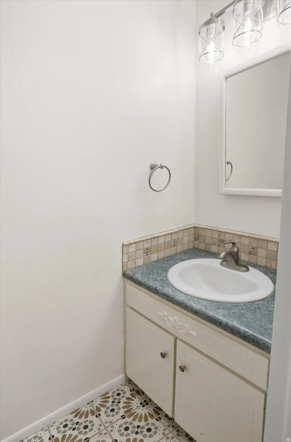 Bathroom vanity featuring a drop-in sink, gray countertop, mosaic tile backsplash, and decorative flooring