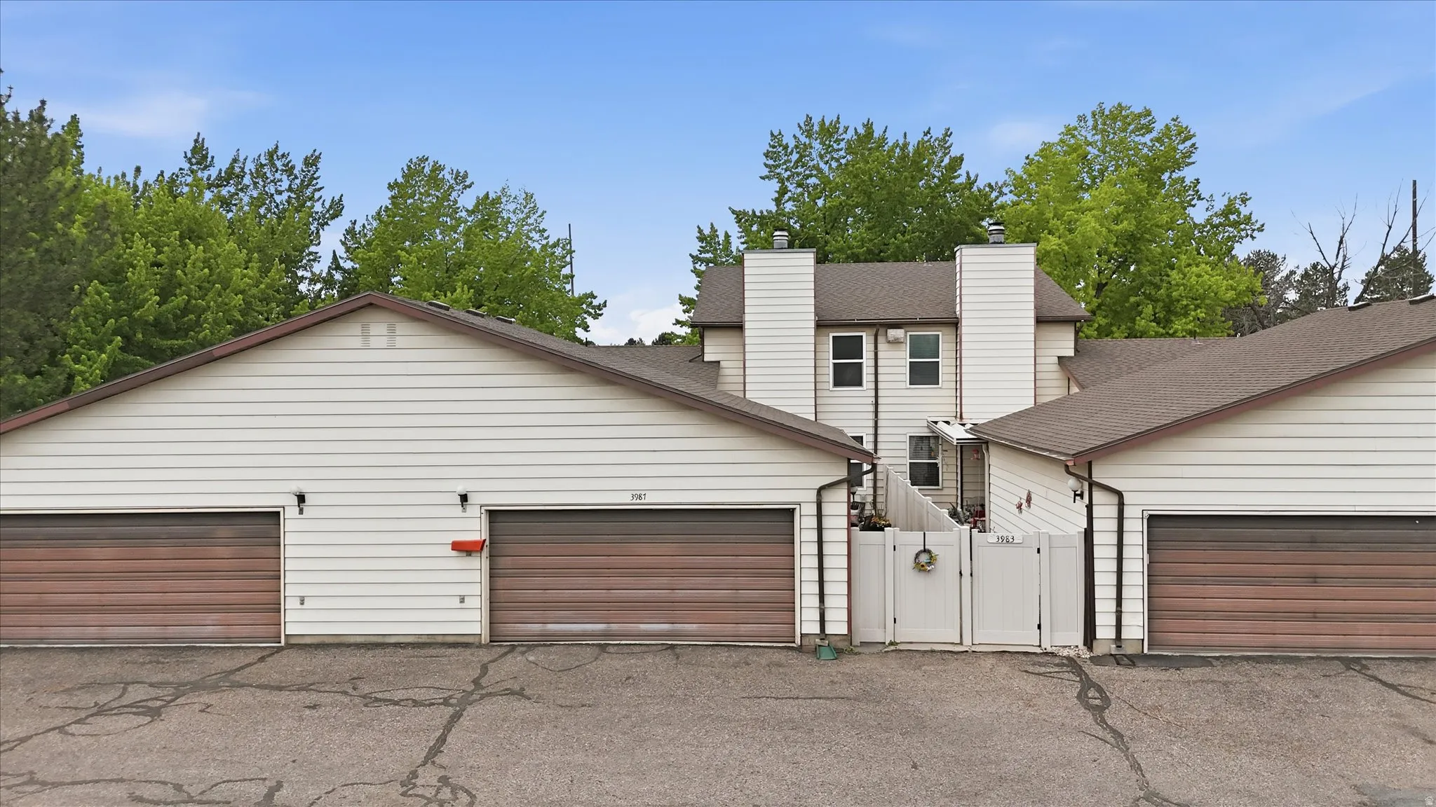 Townhome exterior featuring white siding, brown garage doors, and a partial privacy fence