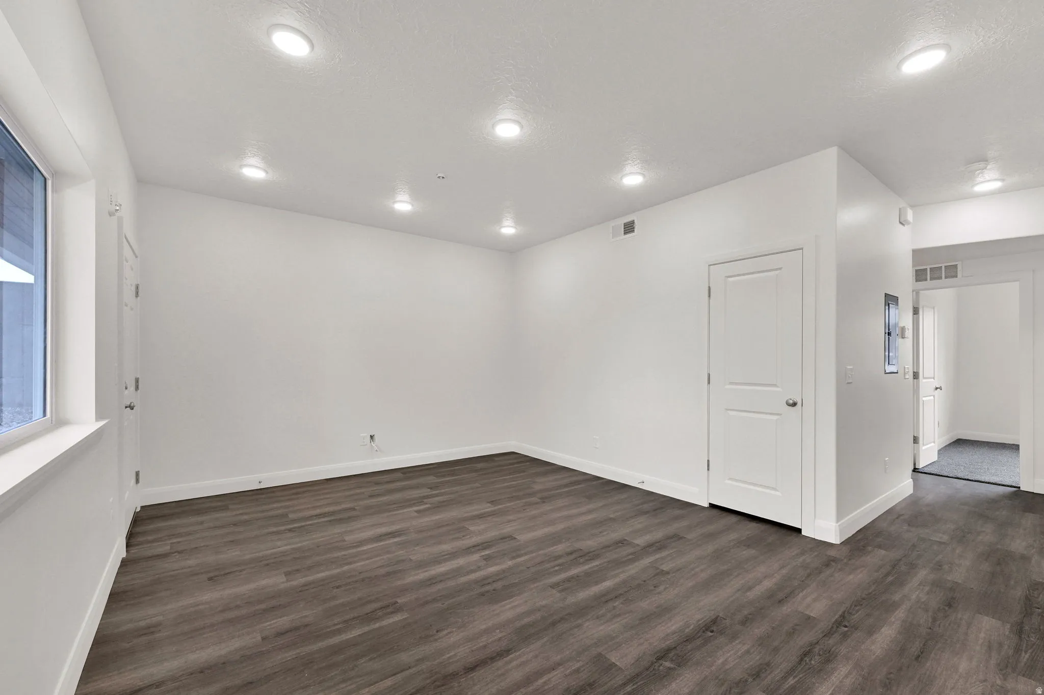 Spacious room featuring wood-finish flooring, recessed lighting, white trim, a solid panel interior door, and a large window