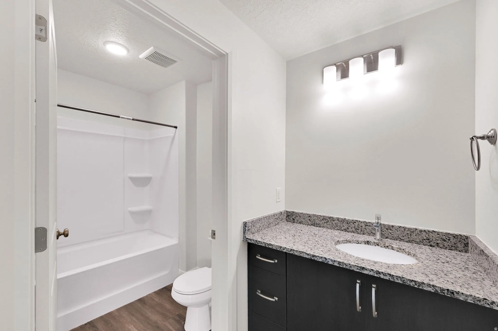 Modern bathroom featuring a dark wood-finish vanity with a light speckled countertop, under-mount sink, and chrome faucet