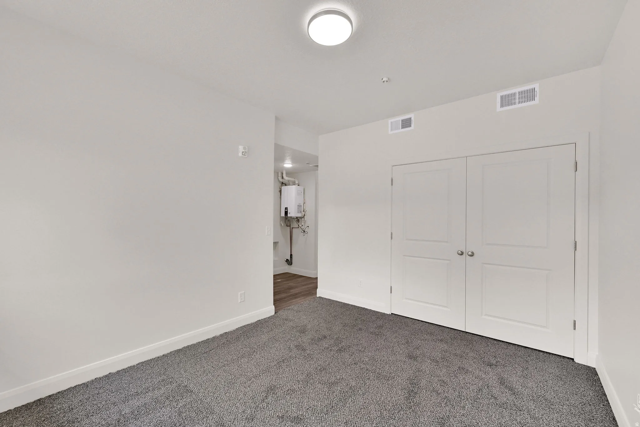 Wall-to-wall carpeting in a neutral tone, white baseboards, and a pair of white doors with silver knobs
