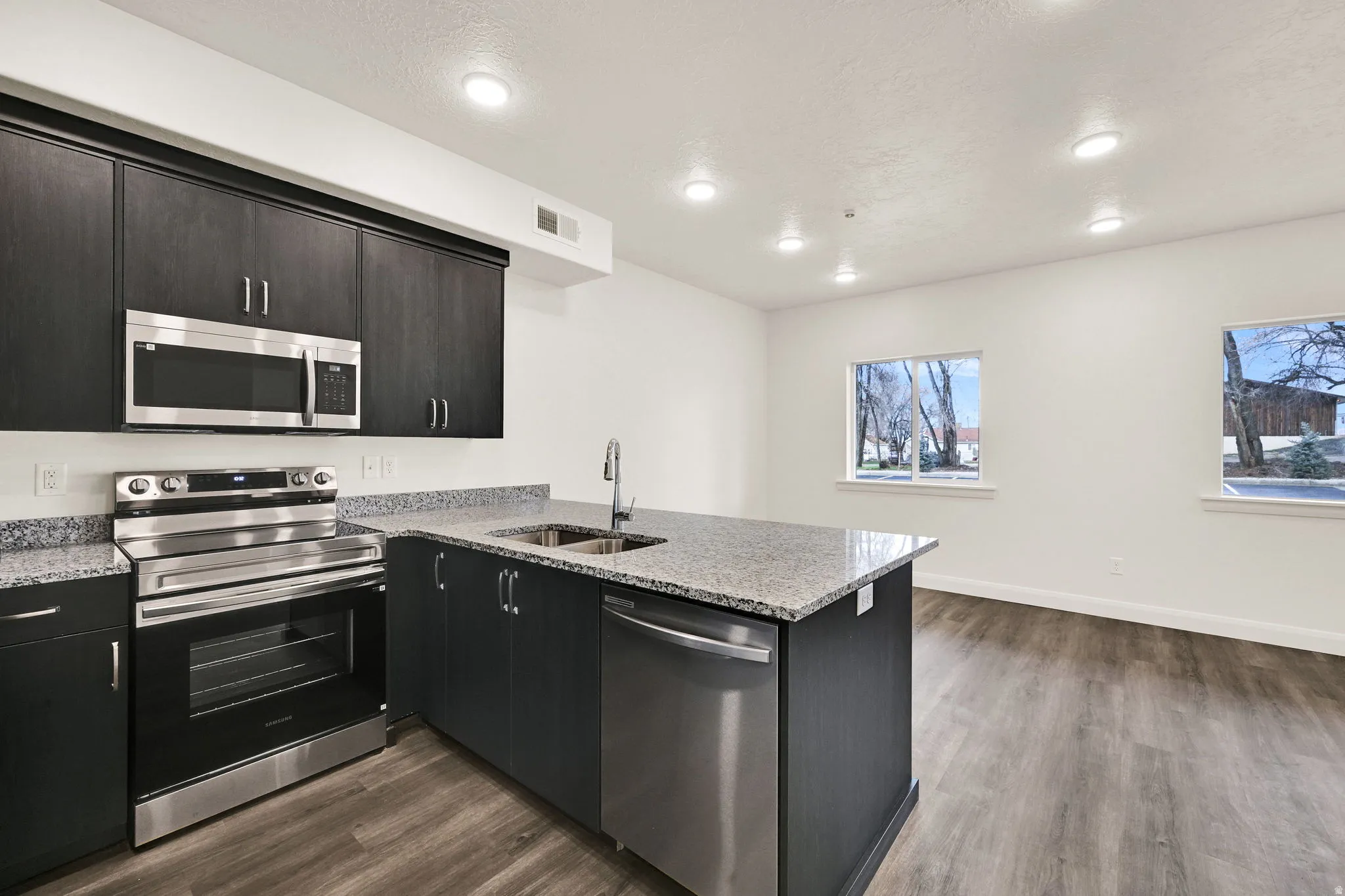 Kitchen island featuring a stainless steel sink and dishwasher, complemented by dark wood-finish cabinetry, granite countertops, and wood-finish flooring