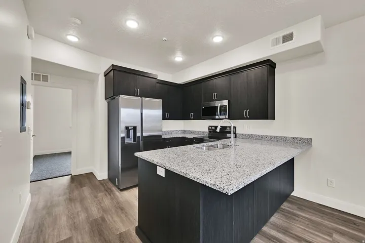 Kitchen featuring dark wood-finish cabinetry, light speckled countertops, stainless steel appliances, and wood-finish flooring