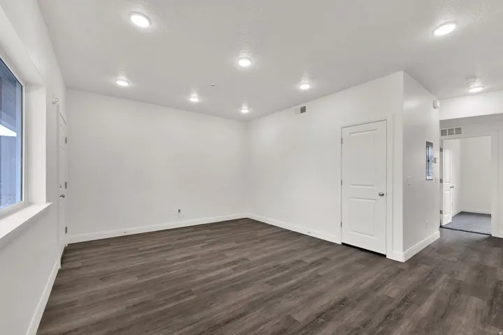 Spacious room featuring wood-finish flooring, recessed lighting, white trim, a solid panel interior door, and a large window