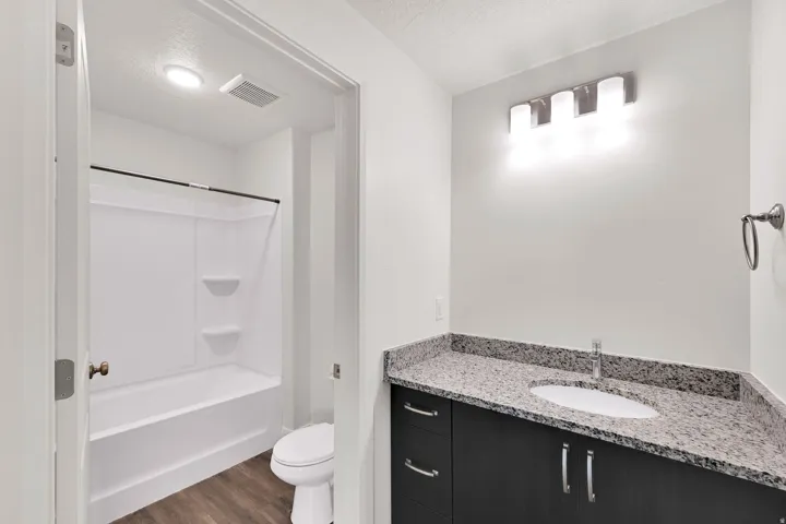 Modern bathroom featuring a dark wood-finish vanity with a light speckled countertop, under-mount sink, and chrome faucet