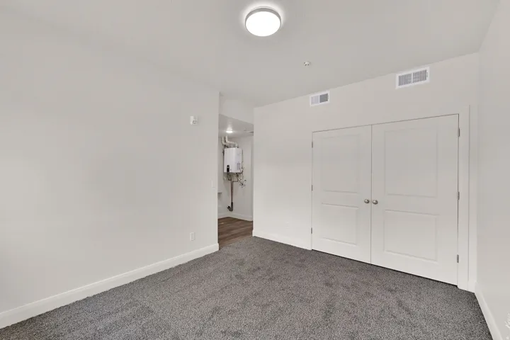 Wall-to-wall carpeting in a neutral tone, white baseboards, and a pair of white doors with silver knobs