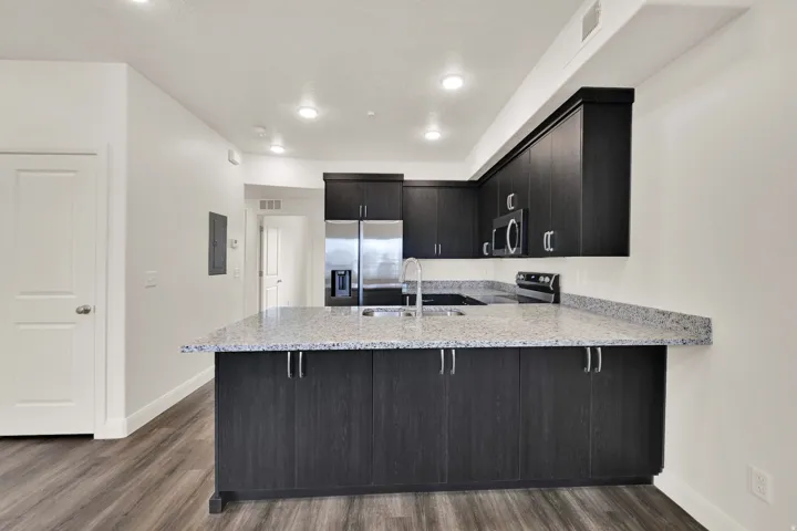 Modern kitchen featuring dark wood-finish cabinetry, light speckled countertops, and stainless steel appliances including a refrigerator, microwave, and range