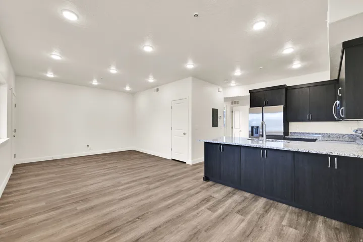 Open-concept living area with wood-finish flooring, recessed lighting, and a kitchen island featuring dark cabinetry and light-toned countertops
