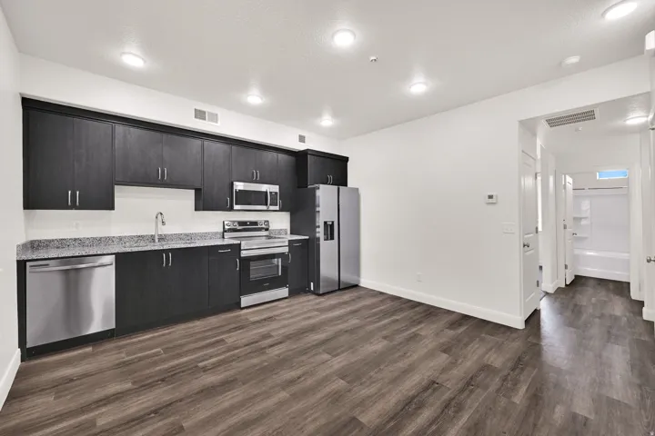 Kitchen featuring dark wood-finish cabinetry with stainless steel hardware, light speckled countertops, a white subway tile backsplash, and stainless steel appliances