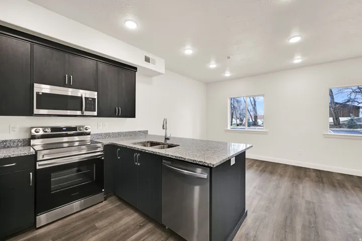 Kitchen island featuring a stainless steel sink and dishwasher, complemented by dark wood-finish cabinetry, granite countertops, and wood-finish flooring