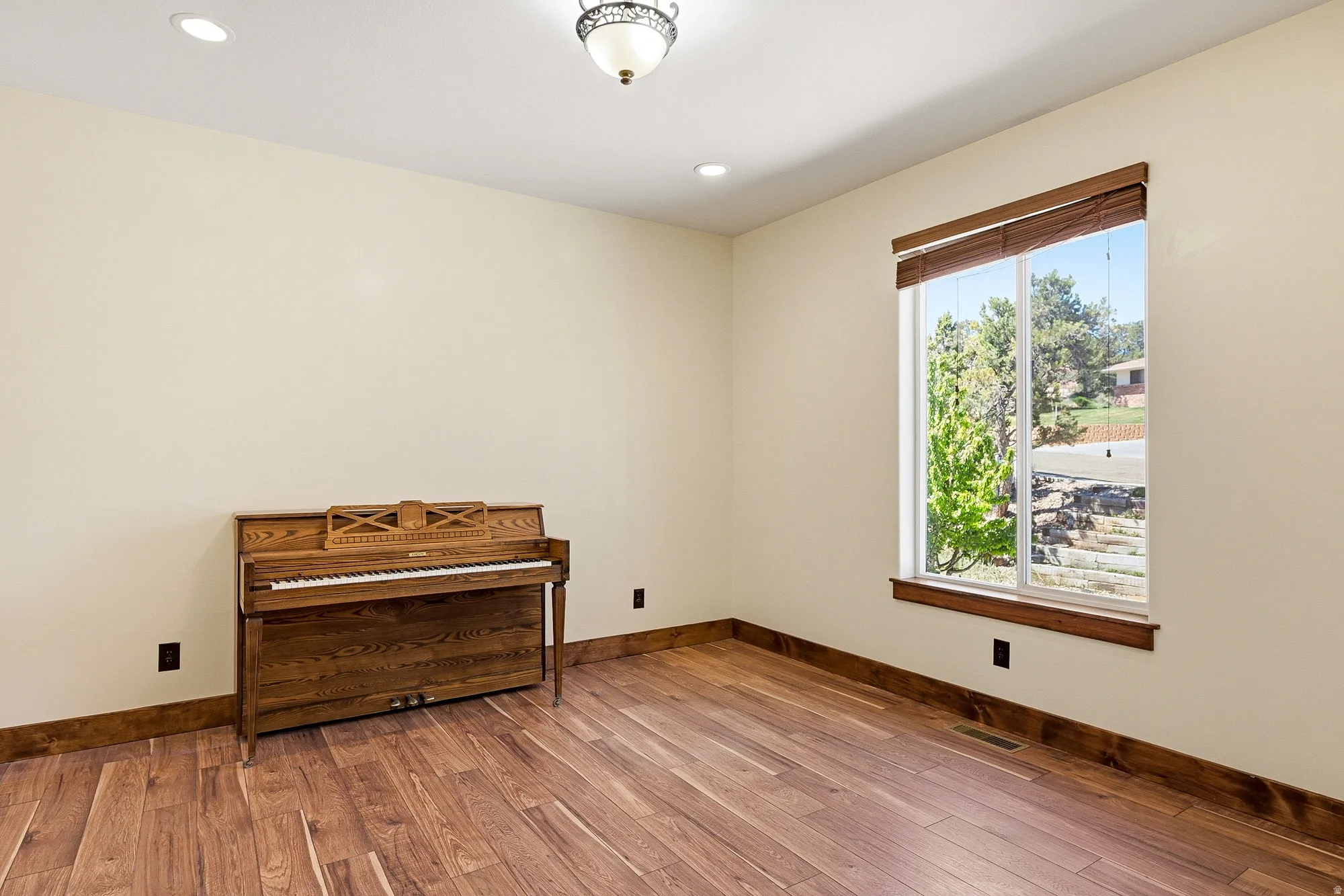 Spacious room featuring wood-finish flooring, recessed ceiling lighting, a large window with wood trim, and a decorative ceiling fixture