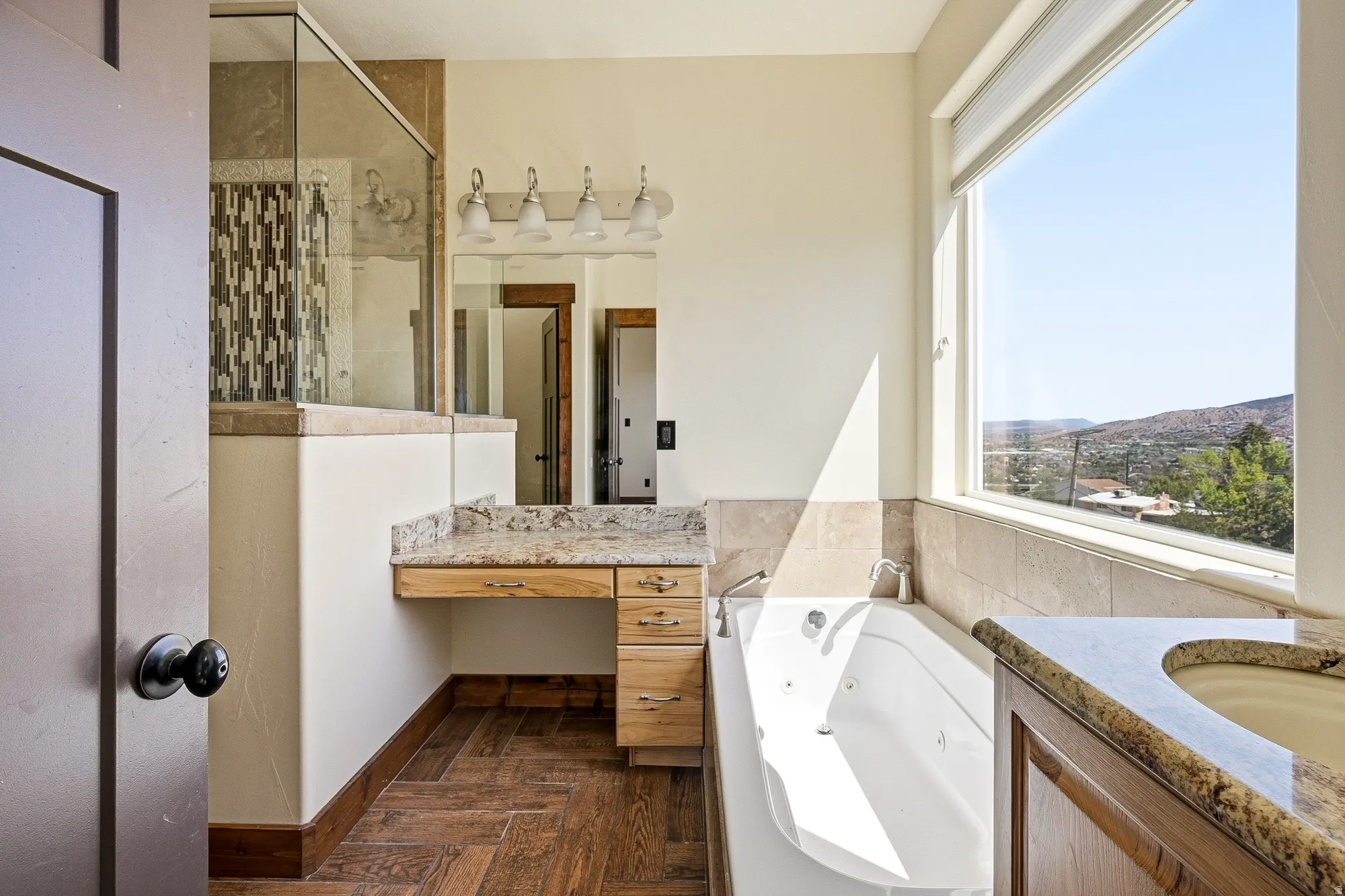 Bathroom featuring a spacious soaking tub, large window, wood-finish flooring, granite countertops, and a glass-enclosed shower with decorative tile